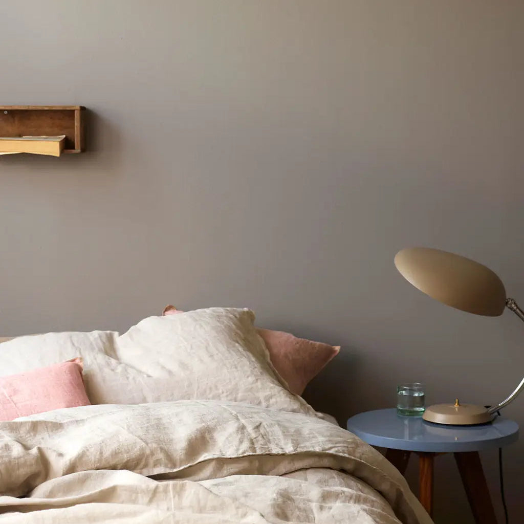 Bedroom with beige bedding, pink pillows, and a side table with a lamp.