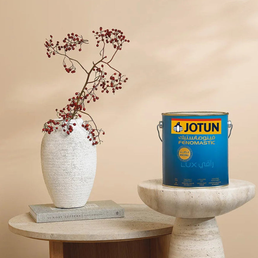 Jotun paint can on a pedestal with a vase and branches against a beige wall